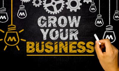 Person holding white chalk with 'GROW YOUR BUSINESS' sign written on the blackboard