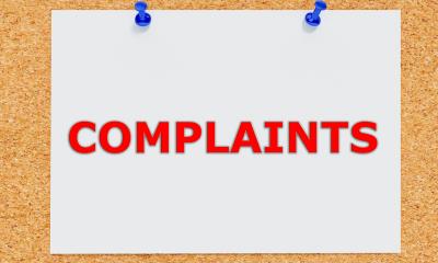 Word 'complaints' written on paper pinned to a wall Sign saying complaints on notice board