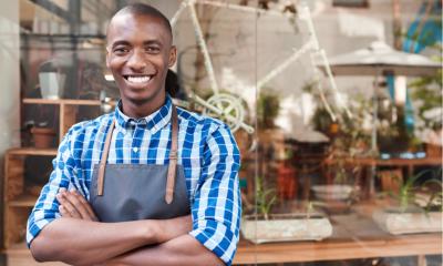 Portrait of a handsome young African entrepreneur smiling and standing with his arms crossed in front of his trendy cafe