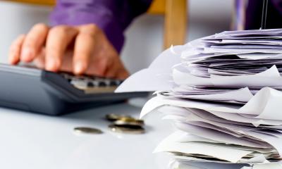 Person budgeting their tax bill using a calculator next to a stack of paper