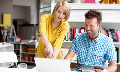 Woman in a yellow shirt pointing to a man in a blue and white plaid shirt's laptop