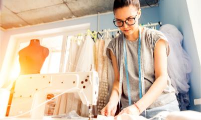 A young dressmaker woman sews clothes on sewing machine.