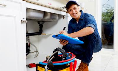 Happy plumber in blue overalls working under a sink