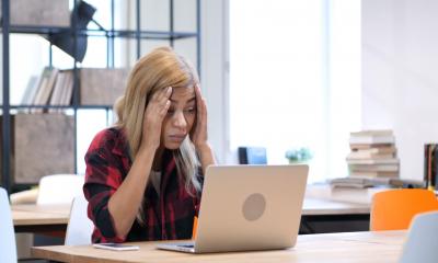 A frustrated woman holds her head in her hands after losing the data on her laptop