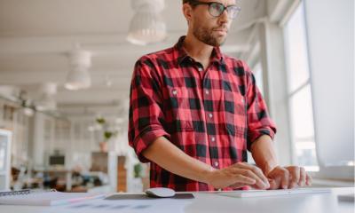 Shot of young man standing at his desk and working on computer