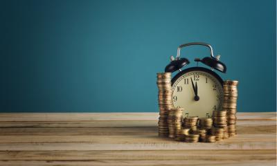 Coins stacked up around an alarm clock on a wooden table