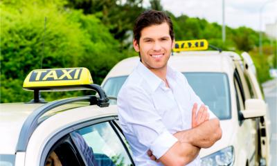 A self-employed taxi driver stands by his car at a taxi rank, waiting for a passenger.
