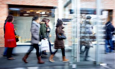 A busy shopping mall entrance with people flowing out the doors
